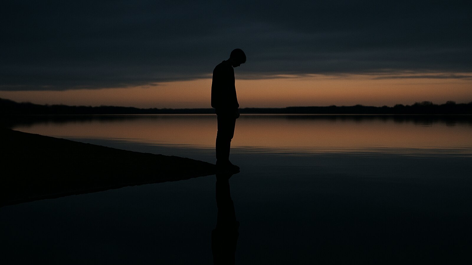 Single silhouette standing at the edge of still water at dusk, their reflection stretching below