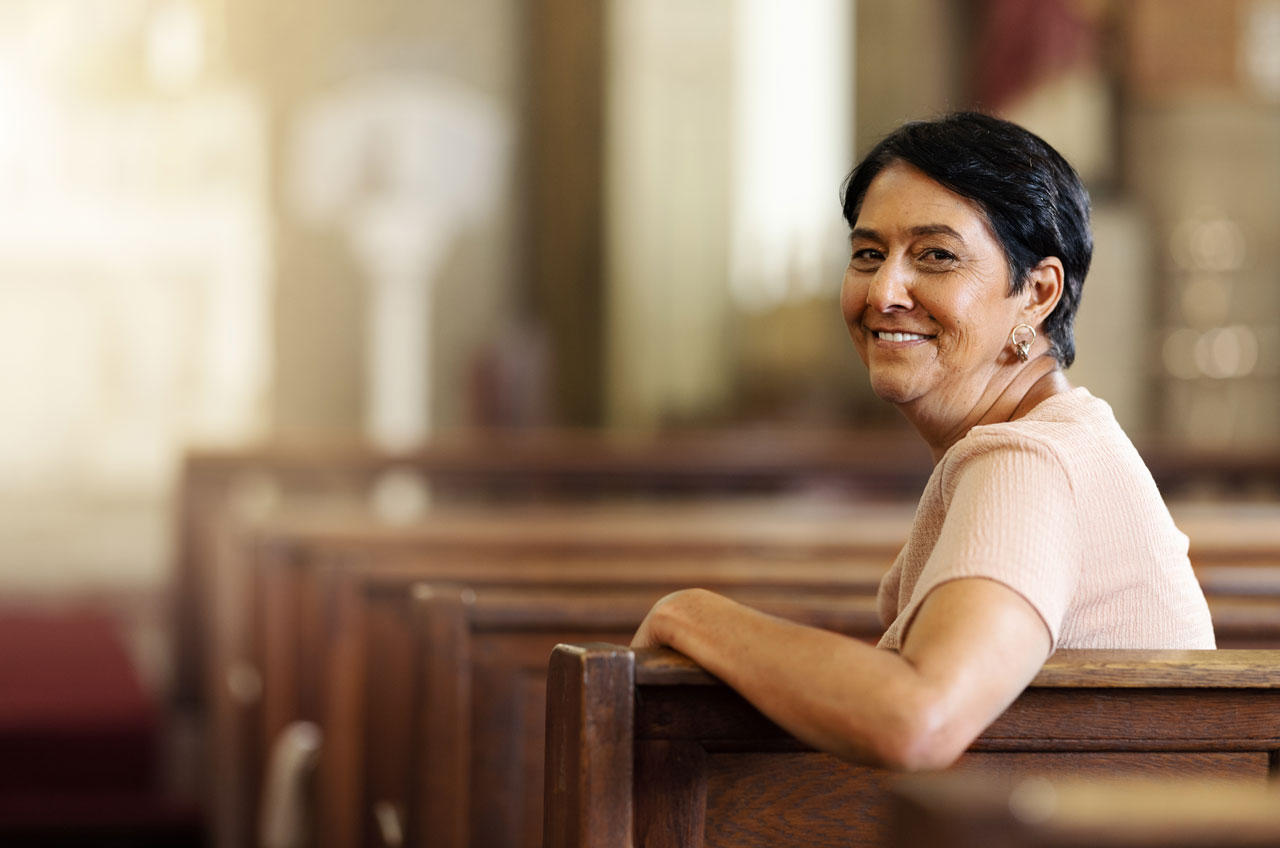 A smiling woman sitting in a church pew, symbolizing hope and reflection.